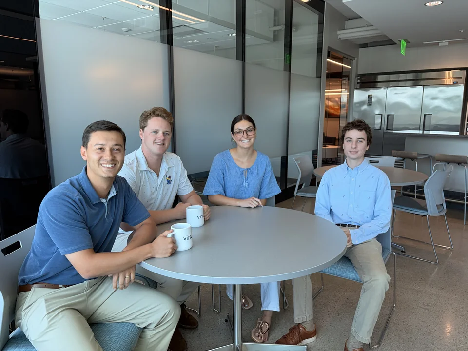 Four people seated around a table with Virtus mugs in the office